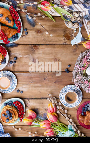 Easter breakfast flat lay with fresh coffee, berries and pastries , orange tulips, croissants with bacon and various sweets , colored quail eggs and s Stock Photo
