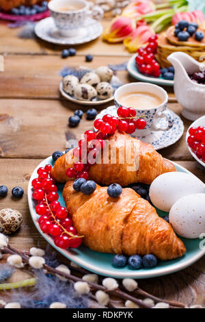 Easter breakfast flat lay with fresh coffee, berries and pastries , orange tulips, croissants with bacon and various sweets , colored quail eggs and s Stock Photo