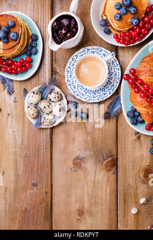 Easter breakfast flat lay with fresh coffee, berries and pastries , orange tulips, croissants with bacon and various sweets , colored quail eggs and s Stock Photo