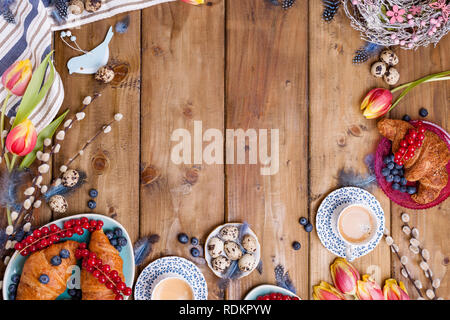 Easter breakfast flat lay with fresh coffee, berries and pastries , orange tulips, croissants with bacon and various sweets , colored quail eggs and s Stock Photo