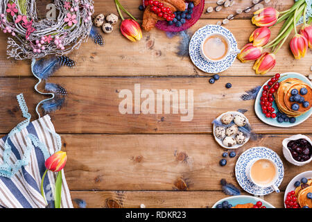 Easter breakfast flat lay with fresh coffee, berries and pastries , orange tulips, croissants with bacon and various sweets , colored quail eggs and s Stock Photo
