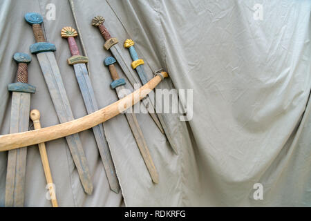 Wooden handmade swords hanging on the rope on grey fabric background. Medieval weapons for close combat displayed on grey fabric texture Stock Photo