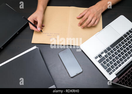 Overhead view of office table with mans hands writing to do list with pen on vintage notebook, computer keyboard, tablet pc and smartphone. copy space Stock Photo