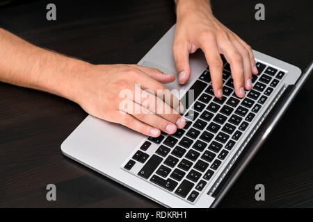 A man is working by using a laptop computer on vintage wooden table. Hands typing on a keyboard. Top view, business office workplace Stock Photo