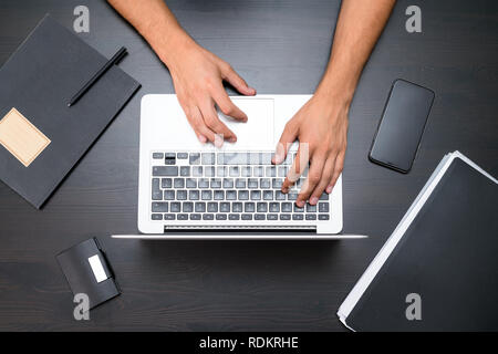 A man is working by using a laptop computer on vintage wooden table. Hands typing on a keyboard. Top view, business office workplace Stock Photo