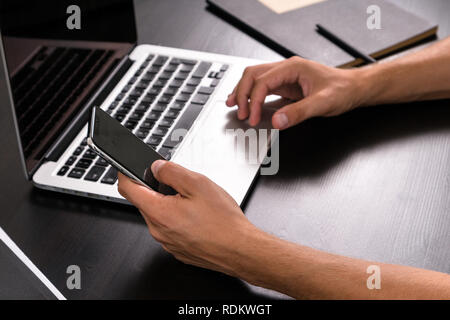 Mans hands typing on smart phone while working on laptop computer on vintage wooden table. Hands typing on a keyboard. Top view, business office workp Stock Photo