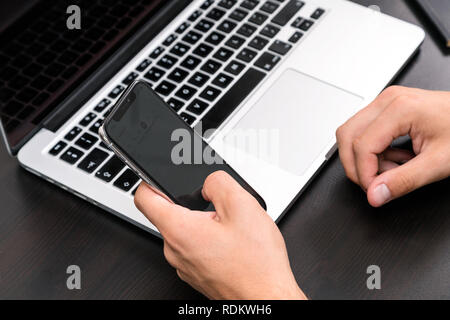 Mans hands typing on smart phone while working on laptop computer on vintage wooden table. Hands typing on a keyboard. Top view, business office workp Stock Photo