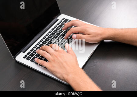 A man is working by using a laptop computer on vintage wooden table. Hands typing on a keyboard. Top view, business office workplace Stock Photo