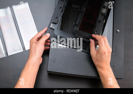Professional technician hand scanning negative film and slides, digitizing old analog photography film technology, workplace on vintage wooden table Stock Photo