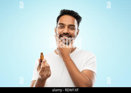 smiling indian man applying grooming oil to beard Stock Photo