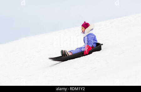 happy little girl sliding down on sled in winter Stock Photo