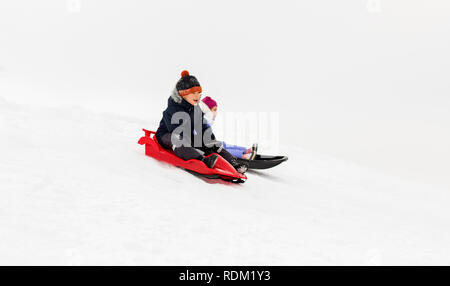happy boy sliding down snow hill on sled outdoors in winter, sledging and  season concept Stock Photo