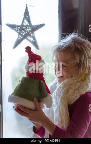 lovely blond girl sitting by the window with christmas toy Stock Photo
