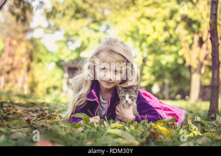 lovely blond girl with cat and lying together on grass in autumn time Stock Photo