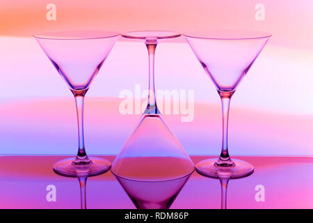 A row of three cocktail / martini glasses in a row with a rainbow of multicolored light painting behind them Stock Photo