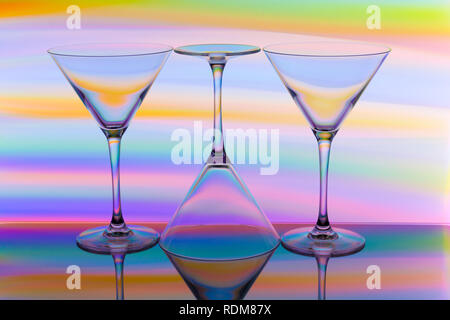 A row of three cocktail / martini glasses in a row with a rainbow of multicolored light painting behind them Stock Photo
