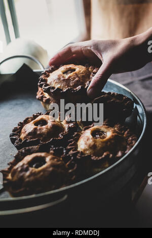 High angle close up of human hand placing freshly baked pies on a tray. Stock Photo