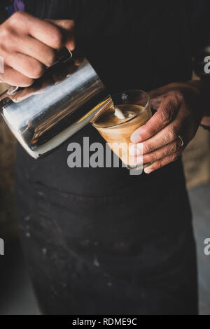 Close up of barista pouring milk from jug into glass, creating foam pattern. Stock Photo