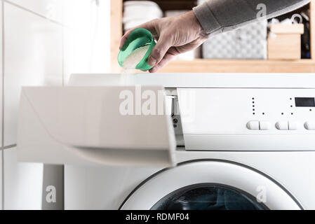 person using dosing aid to pout laundry detergent powder into washing machine Stock Photo