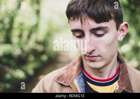 Portrait of young man with short brown hair wearing brown jacket standing in forest. Stock Photo