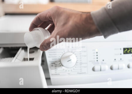person using dosing aid to fill fabric softener into washing machine Stock Photo