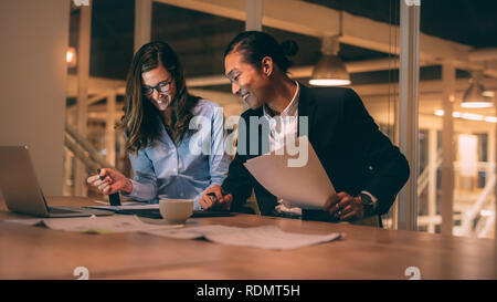 Smiling business partners working together sitting in office. Young entrepreneurs discussing work and working on laptop sitting in office. Stock Photo