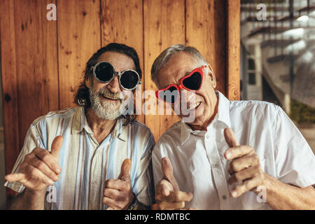Senior men wearing funny sunglasses looking at camera. Happy elderly friends with crazy eyewear with funky gestures. Stock Photo