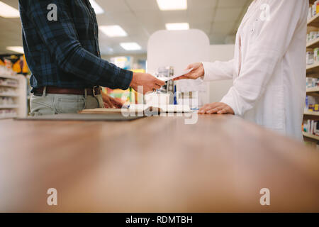 Cropped shot of male customer giving medical prescription to chemist. Side view of male customer buying medicine at drugstore. Stock Photo