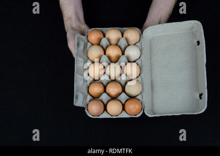 Male hands holding a cardboard egg box full of hen eggs on black felt background. Stock Photo