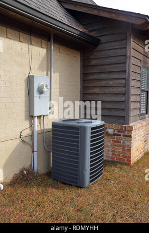 Gray Air Conditioner condenser compressor unit next to painted brick house. Stock Photo