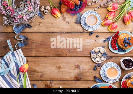 Easter breakfast flat lay with fresh coffee, berries and pastries , orange tulips, croissants with bacon and various sweets , colored quail eggs and s Stock Photo