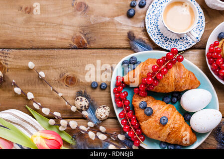 Easter breakfast flat lay with fresh coffee, berries and pastries , orange tulips, croissants with bacon and various sweets , colored quail eggs and s Stock Photo