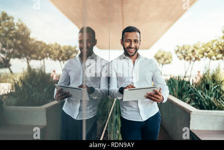 Indian man standing next to glass building with reflection Stock Photo