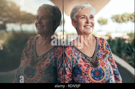 Portrait of a beautiful grey haired middle aged woman looking out into the distance with her reflection Stock Photo