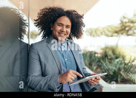 Young mixed race guy with curly afro looking into camera holding and pointing to a tablet Stock Photo
