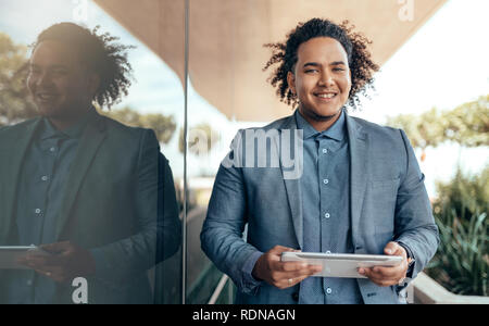 Young mixed race guy with curly afro smiling and looking into camera holding a tablet Stock Photo