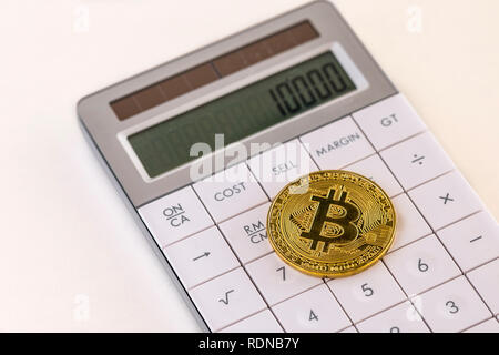 Golden bitcoin on white calculator and cream table Stock Photo