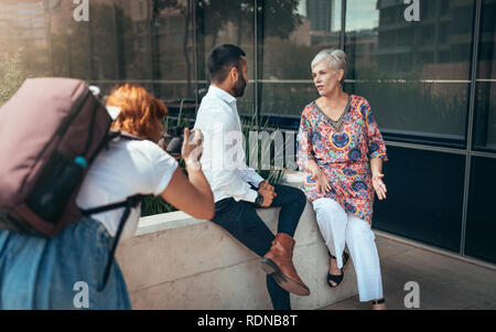 Young female photographer taking photos of two business people sitting outside. behind the scenes Stock Photo
