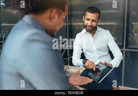 Mixed race and indian businessmen talking and laughing outside next to glass reflective building Stock Photo
