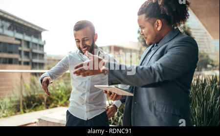 Two trendy businessmen talking and laughing casually outside, talking using hand gestures to show directions or being expressive Stock Photo