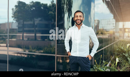 Portrait of a young confident smiling indian man with his arms to his side looking into the camera Stock Photo