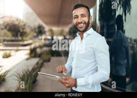 Portrait of a young confident smiling indian man holding a tablet and looking into the distance Stock Photo