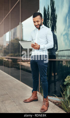 Portrait of a young confident trendy indian man standing and holding a tablet Stock Photo