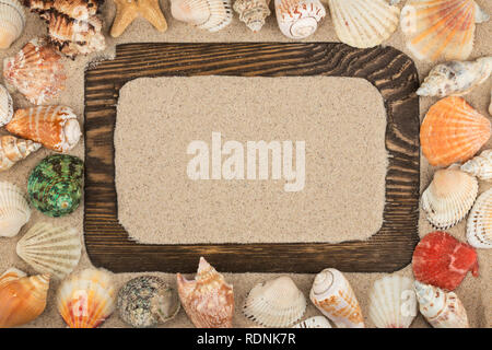 Beautiful wooden frame, stars and seashells on the sand background, with place for your image, text. Top view. Stock Photo