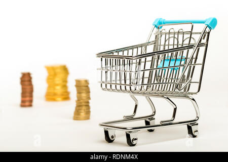 A shopping cart and piles of coins on a white background Stock Photo