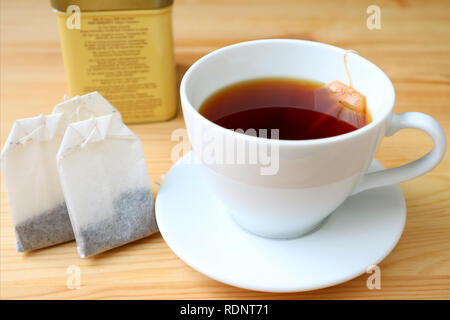 A cup of freshly brewed hot tea with tea bags and blurry tin box on wooden table Stock Photo