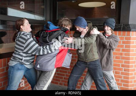 Two boys fighting on the playground while two other teenagers are trying to get them apart, posed scene Stock Photo