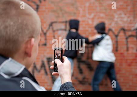 Two boys fighting on the playground while a third films with his cell phone, posed scene Stock Photo