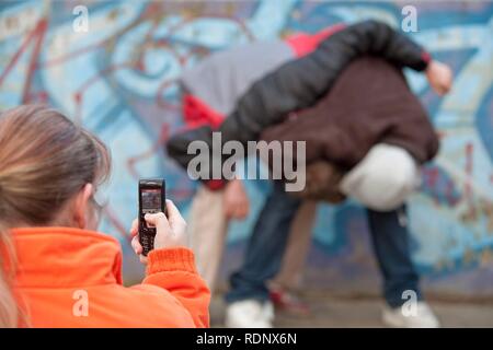 Two boys fighting and being filmed by a girl with her mobile phone, reenactment Stock Photo