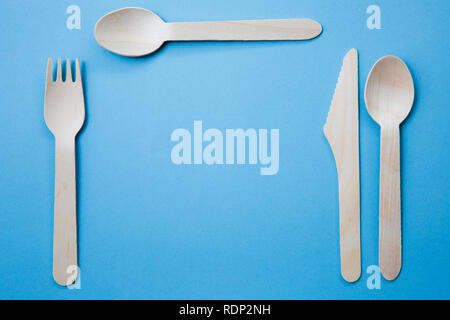 A variety of recyclable wooden cutlery including knife, fork and spoon on a blue background in a place setting with copy space Stock Photo